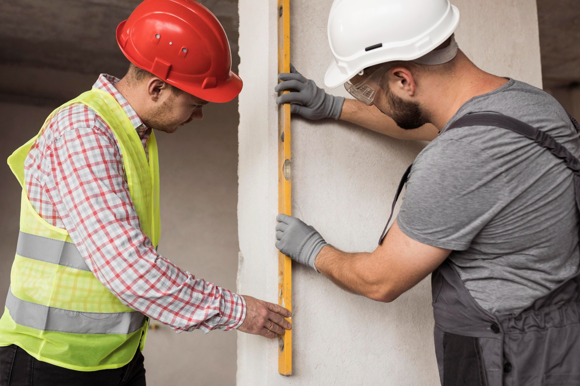 Zwei Handwerker richten gemeinsam eine Wand auf einer Baustelle aus.